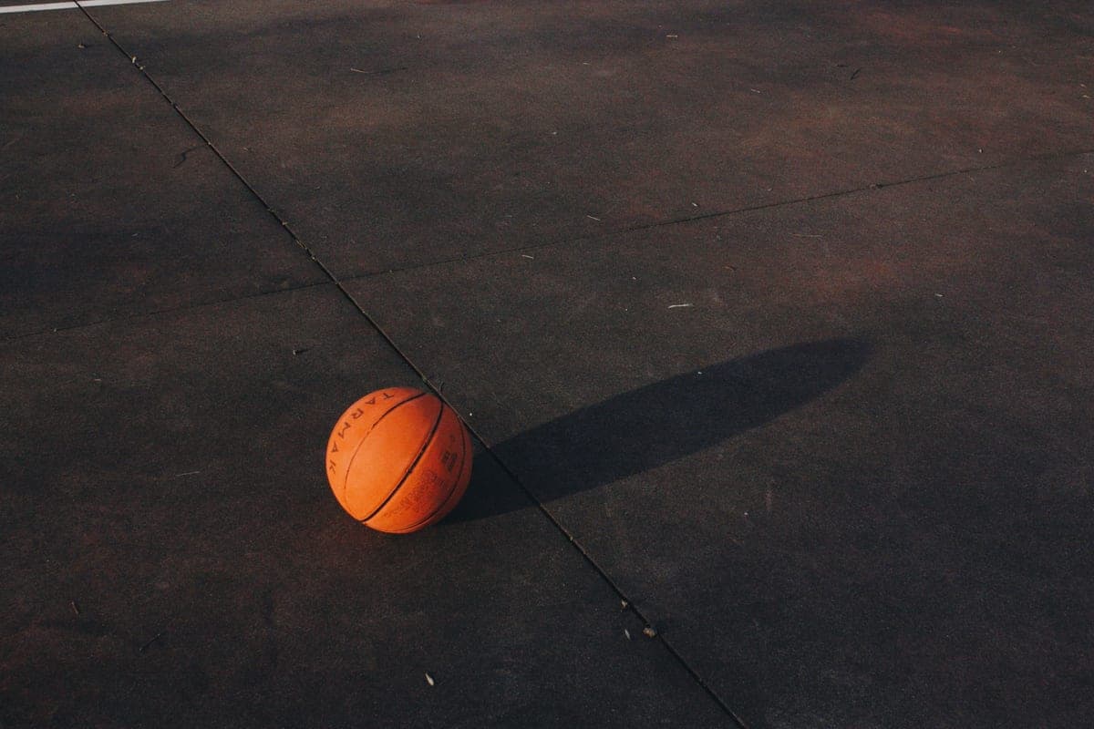 A single basketball casting a long shadow on a textured court at dusk