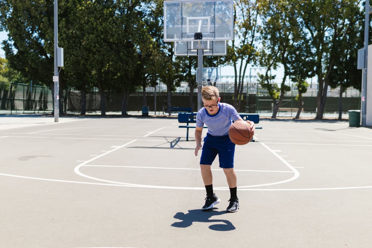 A young boy dribbling a basketball on an outdoor court in bright sunlight