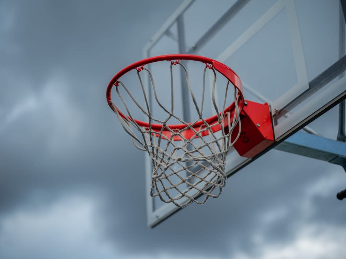 An outdoor basketball hoop and net against a dramatic cloudy sky