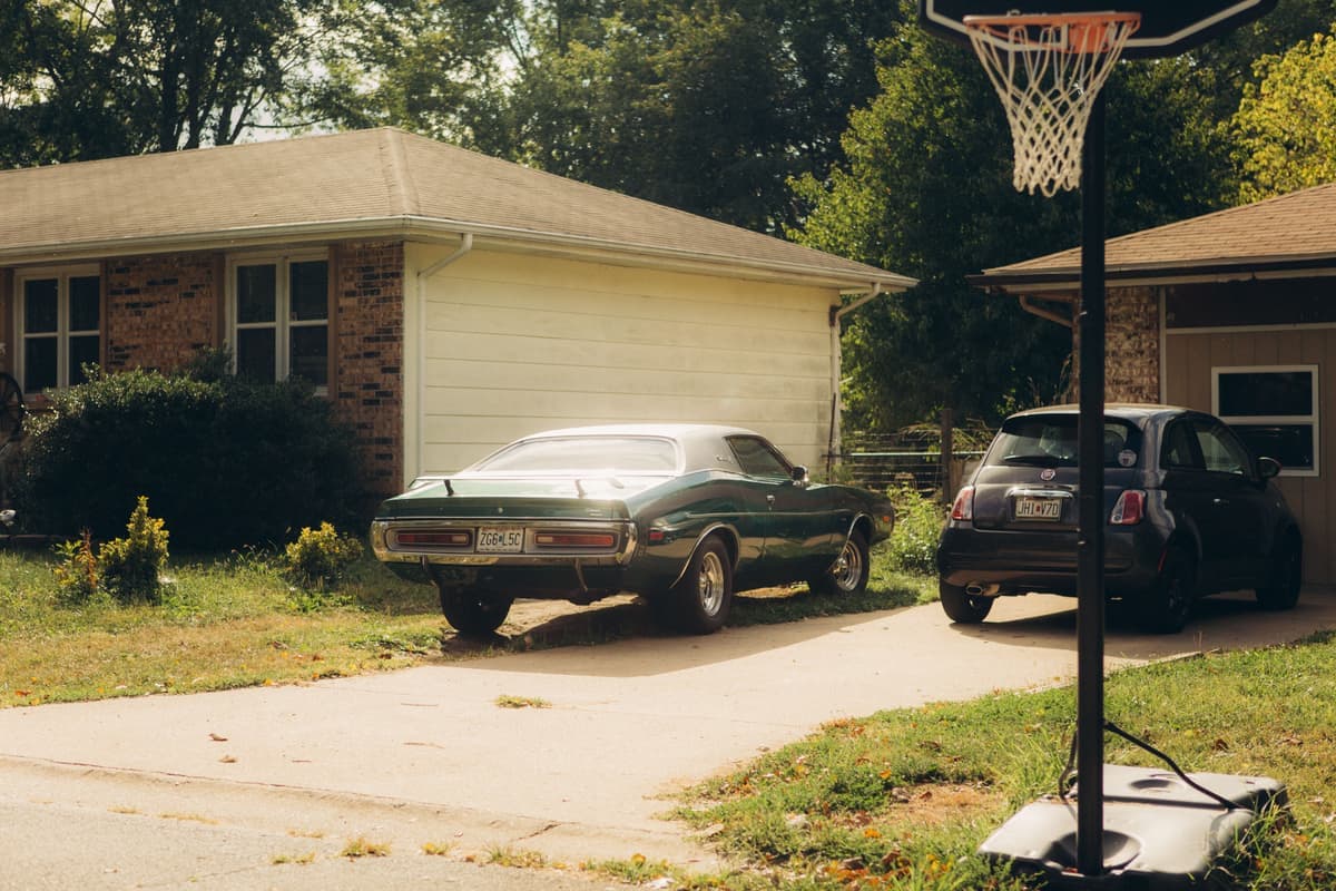 A suburban driveway with a parked car and a basketball hoop under a clear sky