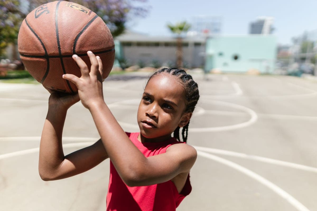 A young child practicing a basketball shot on an outdoor court in bright sun